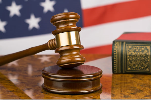 Photograph of a desk with a gavel and block and book with United States flag in the background