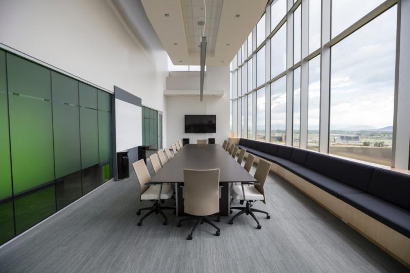 Photograph of a meeting room - large conference table with chairs, white board on wall, television mounted on wall, large bank of windows