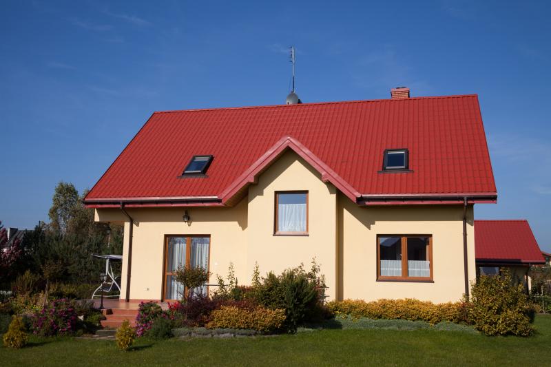 Photograph of a Single Family House (pale yellow with red roof ) with brick steps and porch surrounded with shrubs, flowers, trees, and grass