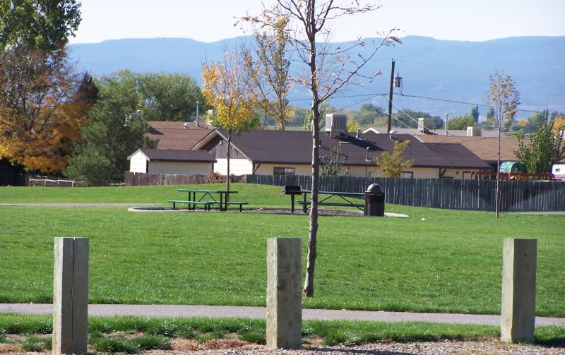 View of two picnic tables and green grass in the foreground, houses and a mountain range in the background