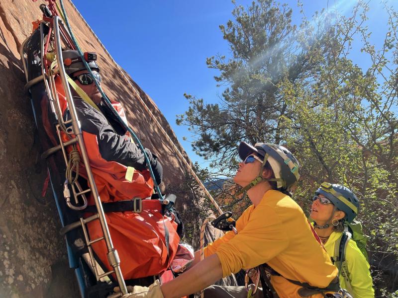 Two individuals position a spine board to be hoisted up a rockface.