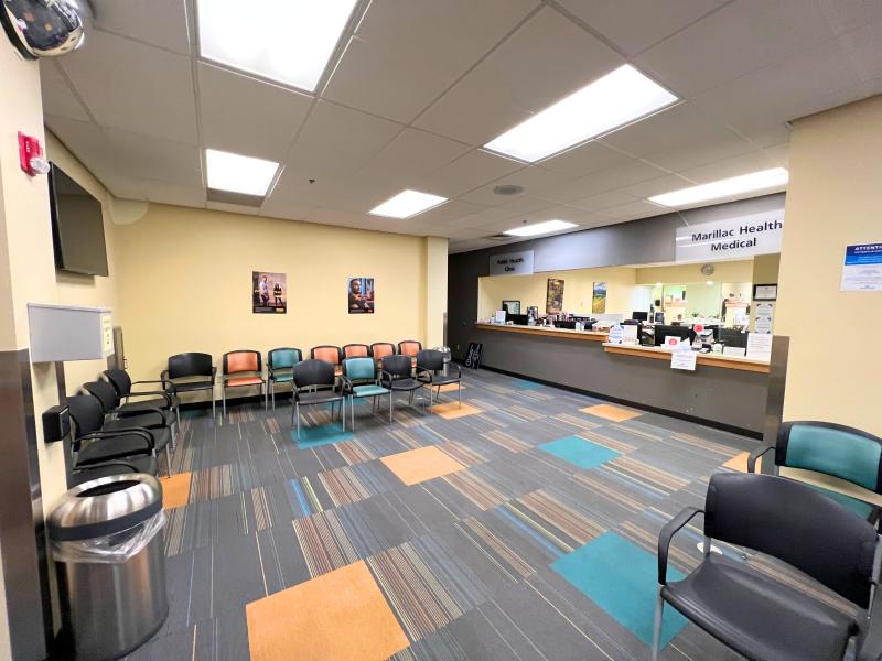 Waiting room with a check in desk along one side, chairs for waiting, and grey multi-colored carpet showing.