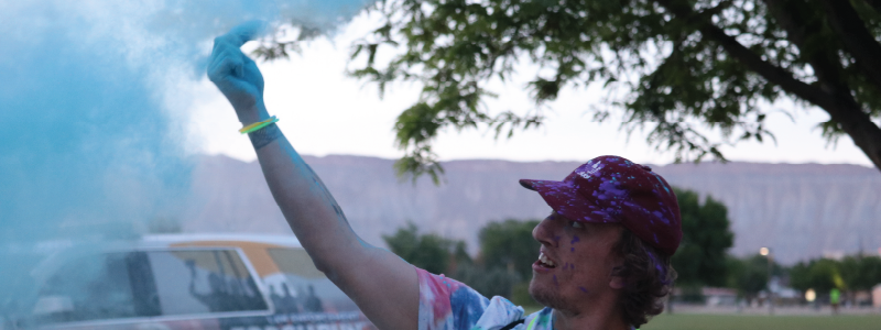 A young man holds his hand in the air releasing glow in the dark blue dust.