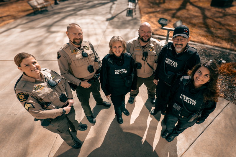 Six Behavioral Health staff members, 3 in Sheriff uniforms and 3 in civilian outfits with vests that display the words Behavioral Health.  