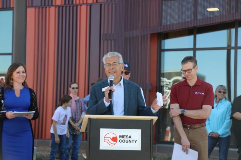 Man standing outside at lectern holding a mic to his mouth. 