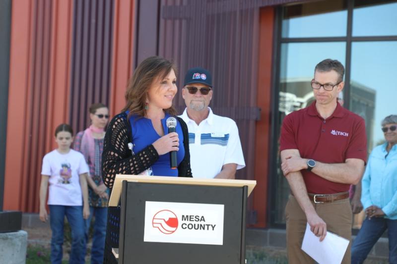 Woman standing outside at lectern holding a mic to her mouth. 