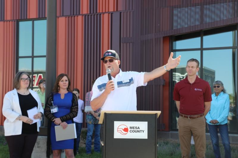 Man standing outside at lectern holding a mic to his mouth. 