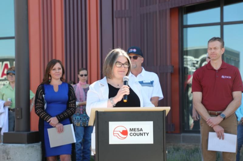 Woman standing outside at lectern holding a mic to her mouth. 