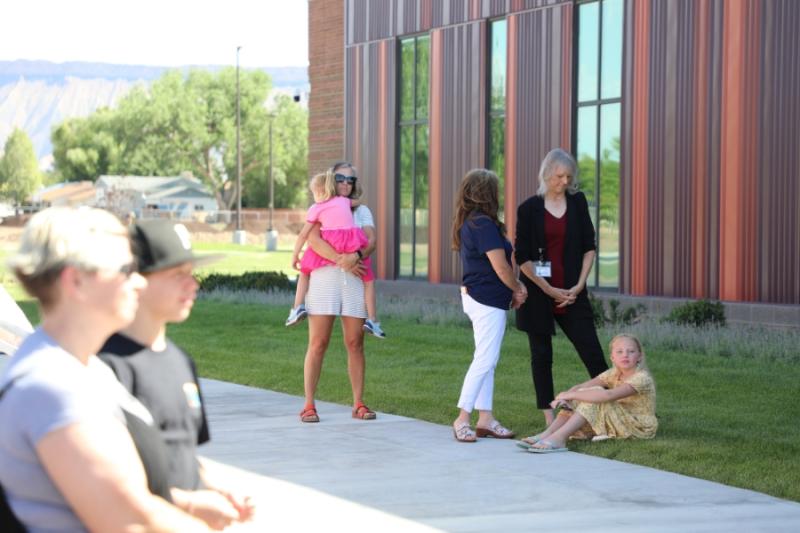 Woman holding child next to other people standing outside at community event. 