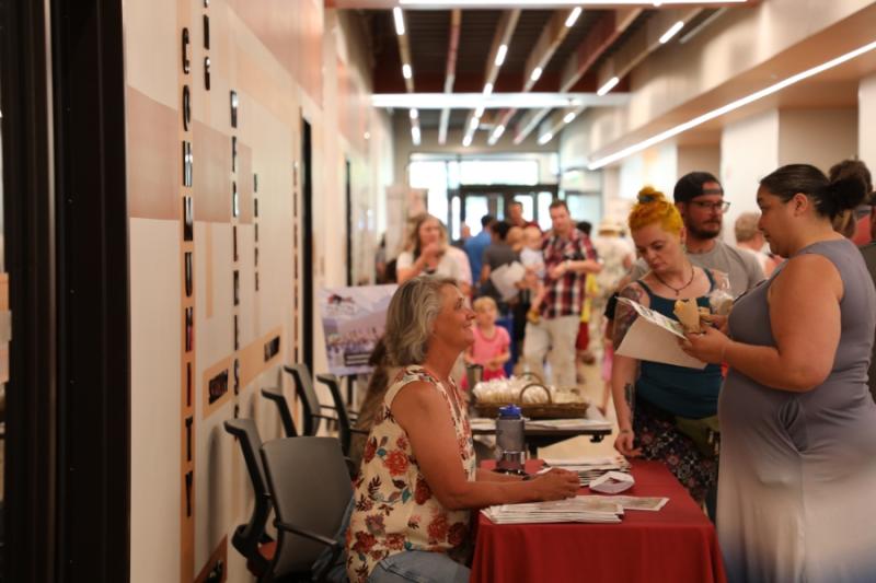 Woman standing at booth talking to a woman sitting at a table. 