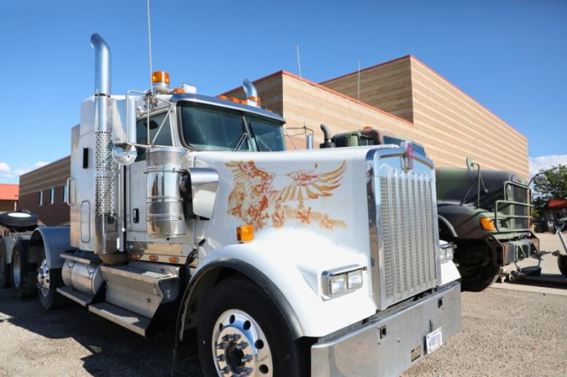 Two large semi trucks. One is white and one is camo. 