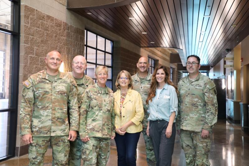 Army soldiers and two civilians smiling at camera. 