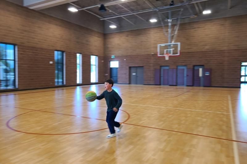 Young boy holding green basketball in open gym. 