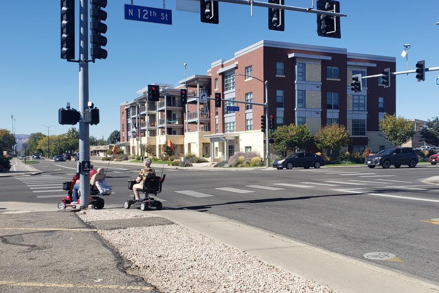 Two pedestrians, each in a wheelchair, preparing to cross 12th Street at Orchard Avenue. 