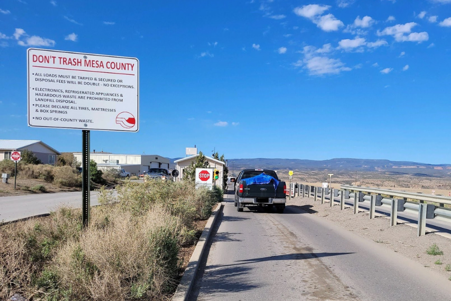 Black Ford truck with blue tarp cover sits at Mesa County Landfill entrance. A sign near entrance booth reads DON'T TRASH MESA COUNTY.