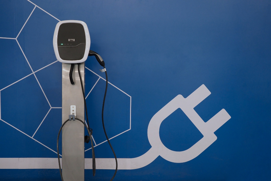 Silver black and white electric vehicle charging station against a blue wall painted with white electrical chord. 