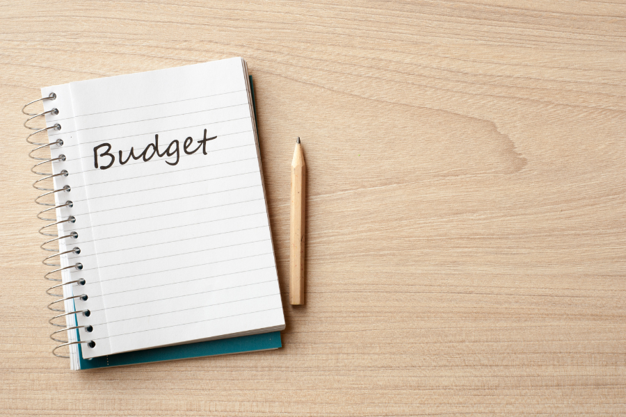 Light wood table with pencil and notepad on top reading "budget".