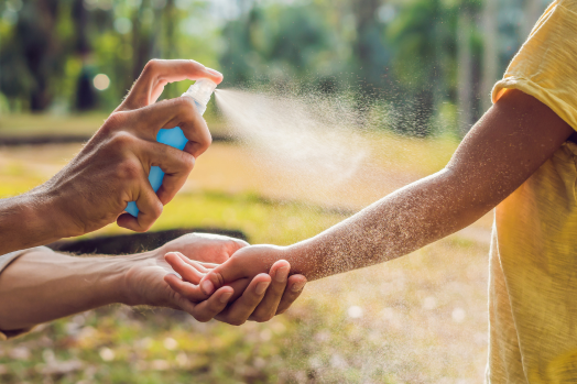 Adult spraying insect repellent on another person's arm. 