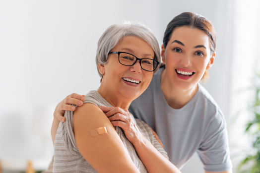 Mother and daughter posing together. Mother has a bandaid on her upper arm, indicating she received a vaccination recently.