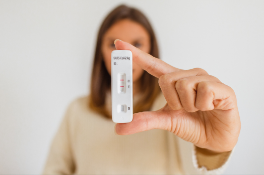 Woman with long, brown hair holding a COVID-19 test kit in her hand.