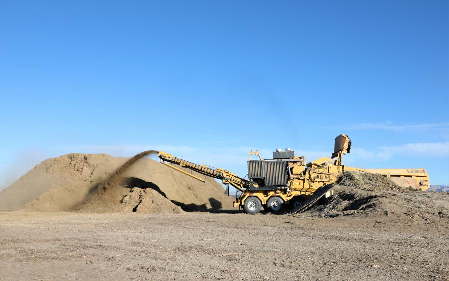 Yellow heavy construction equipment intaking yard waste and spraying out brown compost material. 