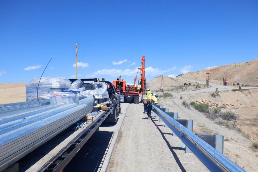 Construction workers in bright yellow clothing working on guardrails next to a large truck holding materials. 