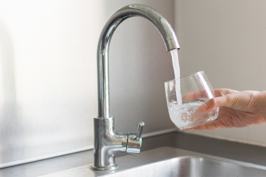 Person filling up a glass of water from a silver faucet.