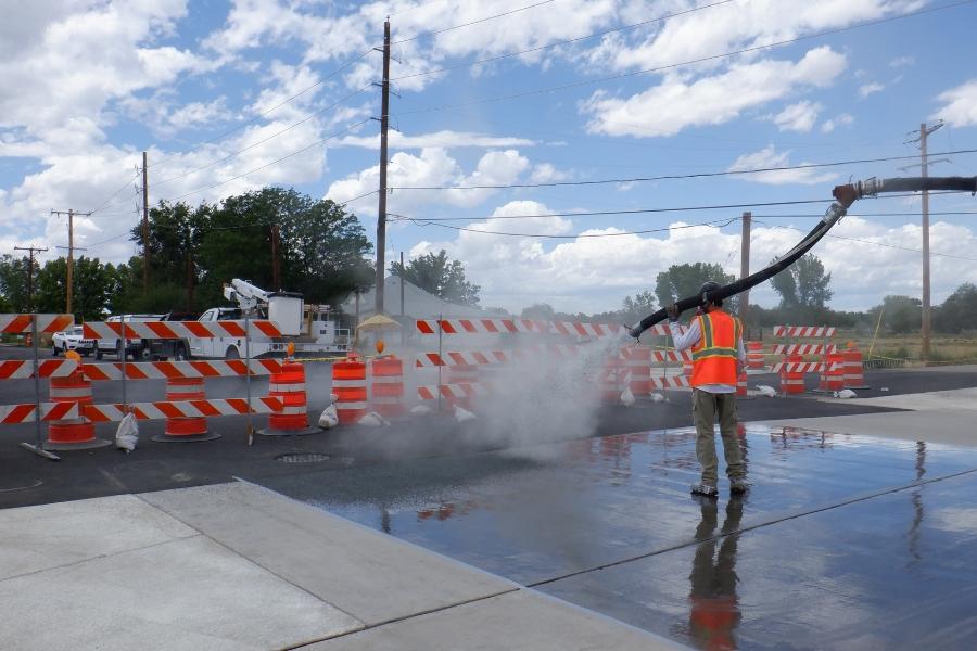 Man in orange vest sprays over construction area. 