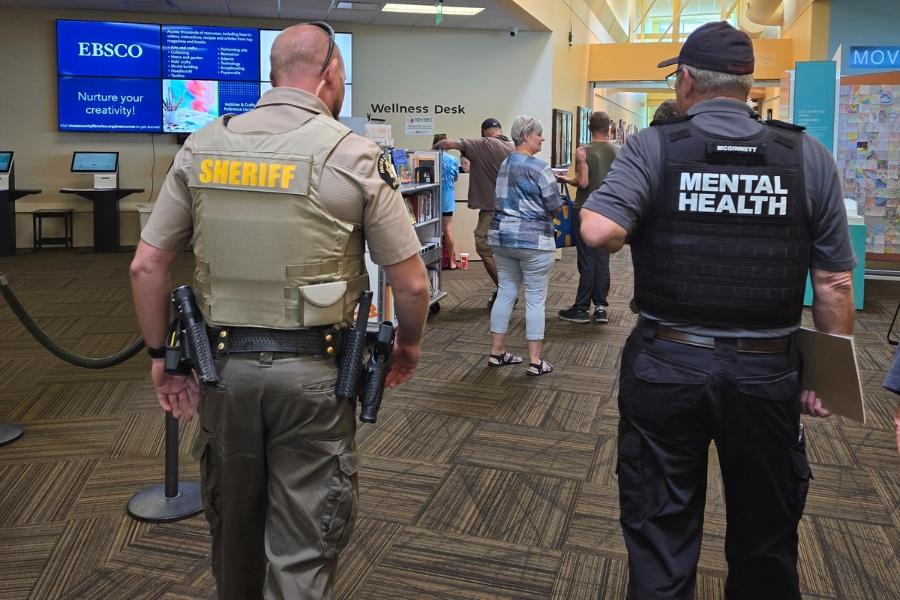 Two men walking away from camera. One man's shirt says, "Sherriff" and the other says, "Mental Health."