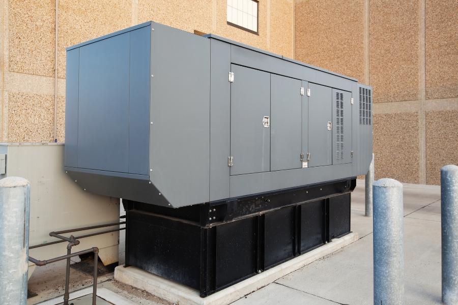 Grey emergency generator outside tan building. 