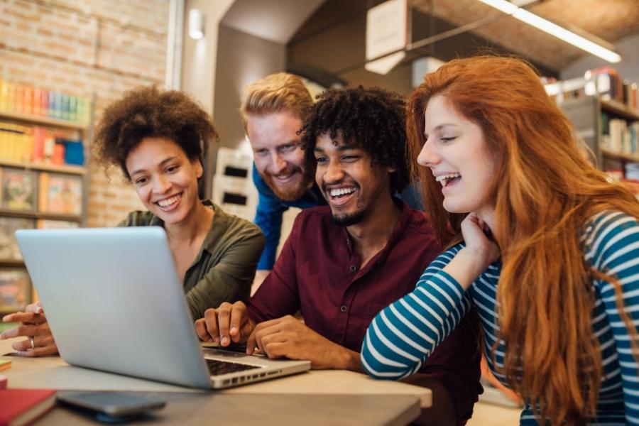 Four young adults looking at silver laptop screen. 