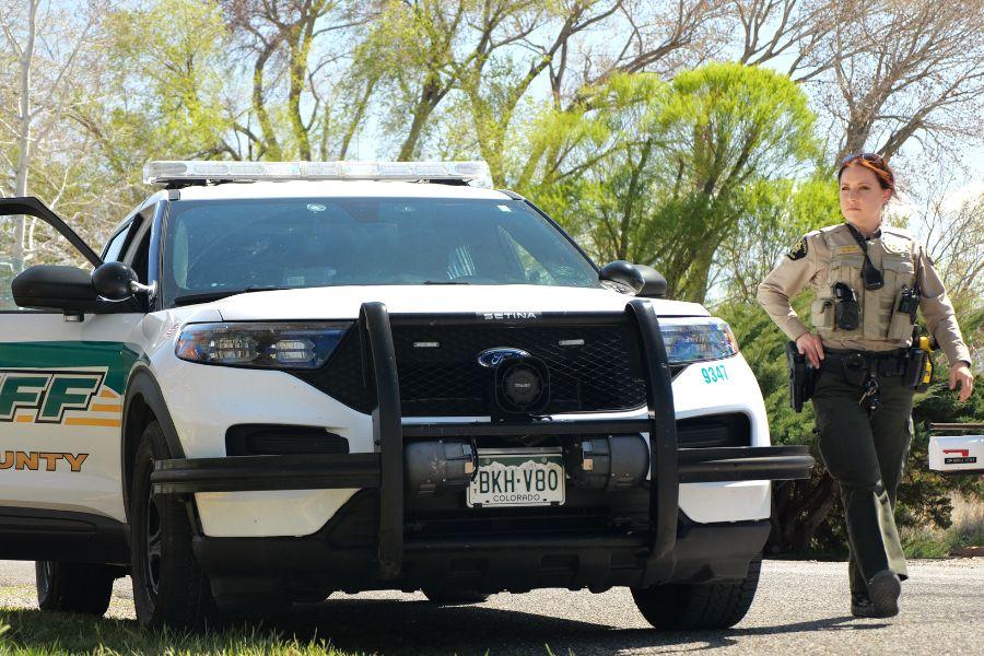 A woman in a sheriff's deputy uniform is standing next to a white and green Mesa County Sheriff’s Office vehicle. 