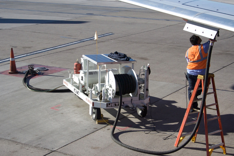 Person in orange vest standing on ladder fueling an airplane. 