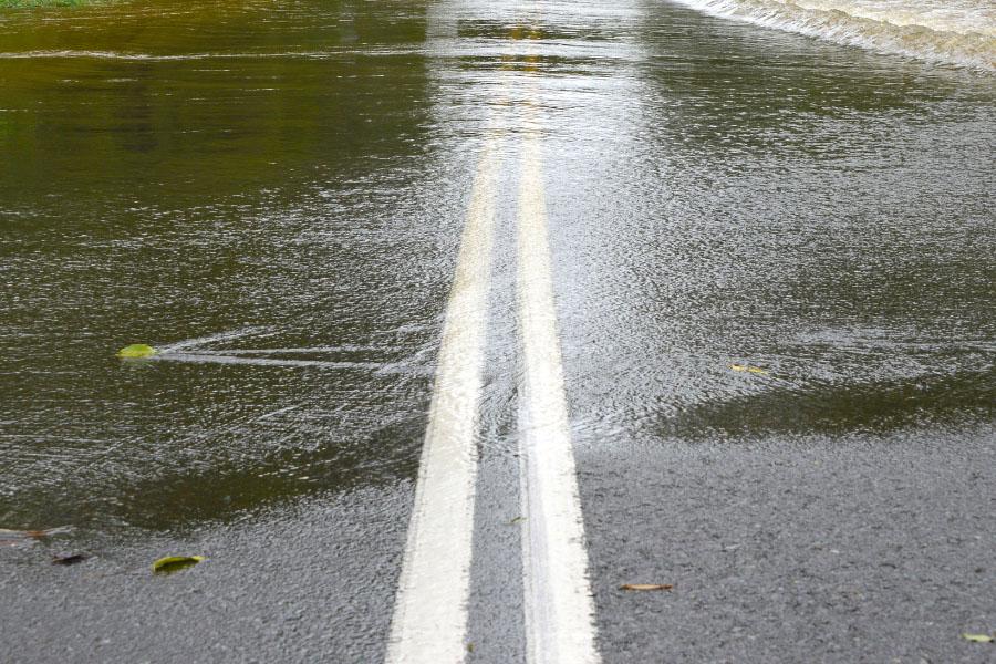 Water rising above black road with two white lines.