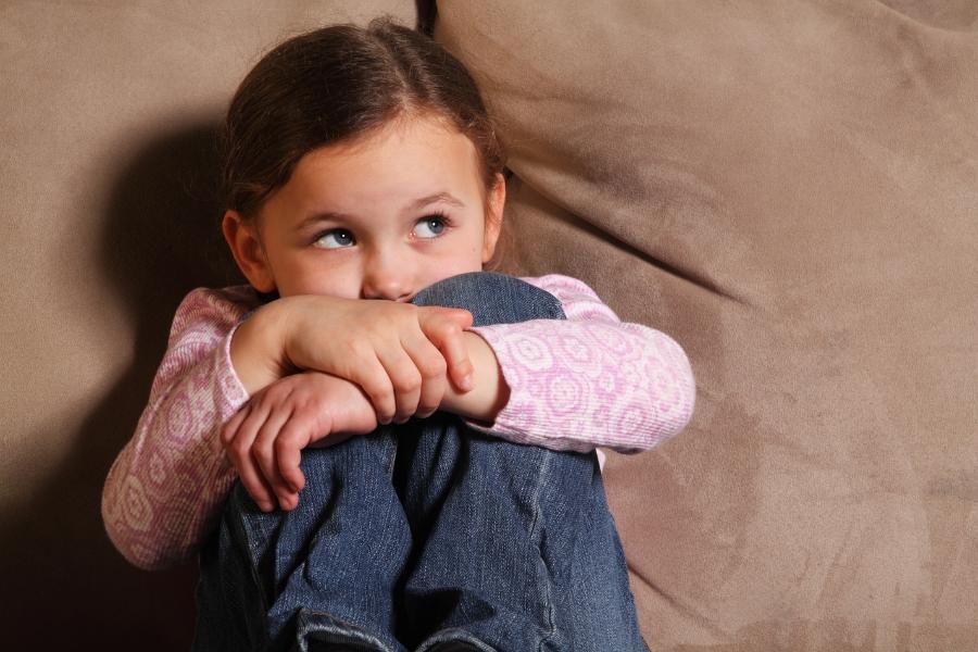 Young girl looking up with her arms wrapped around her knees.