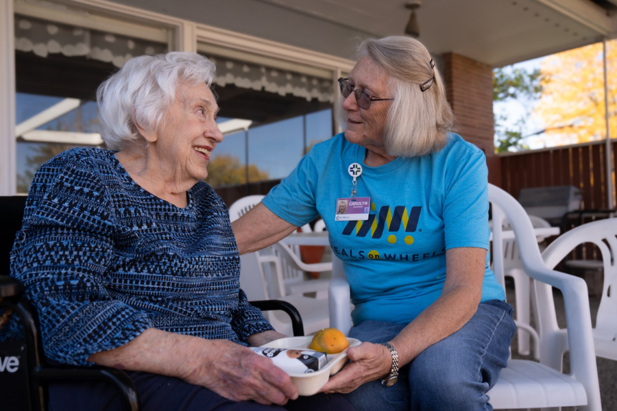 A smiling woman hands an elderly woman a meal.