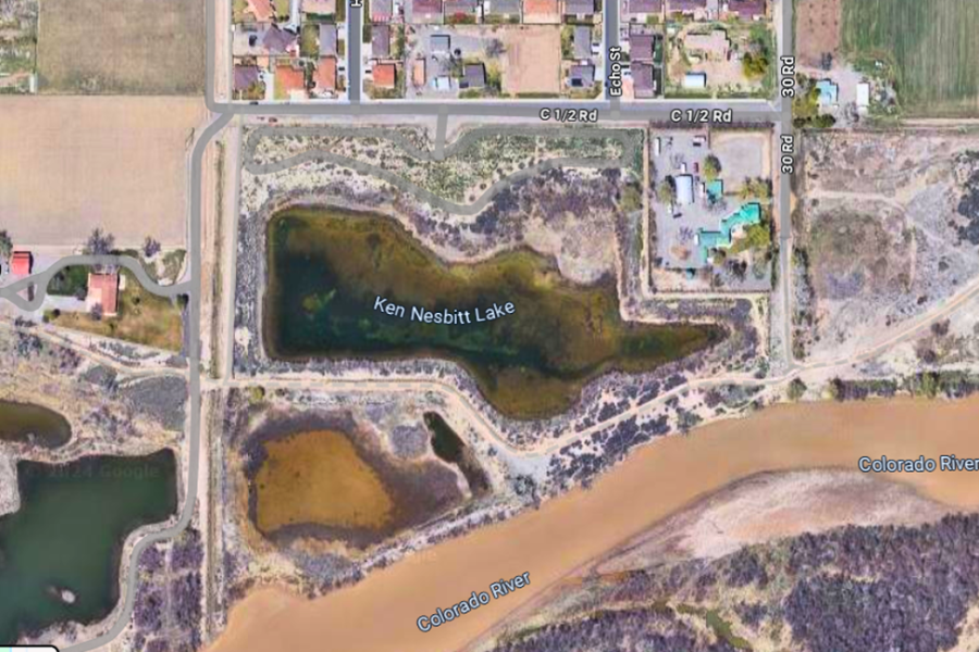 An overhead satellite view of Ken Nesbitt Lake in Mesa County, Colorado, near the Colorado River. It features the lake surrounded by a mix of residential areas and undeveloped land.